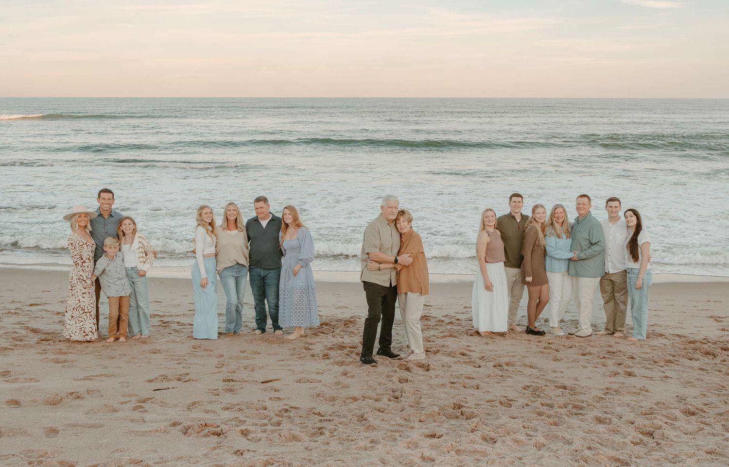 Extended family poses together on a scenic beach at sunset in coordinating neutral outfits.