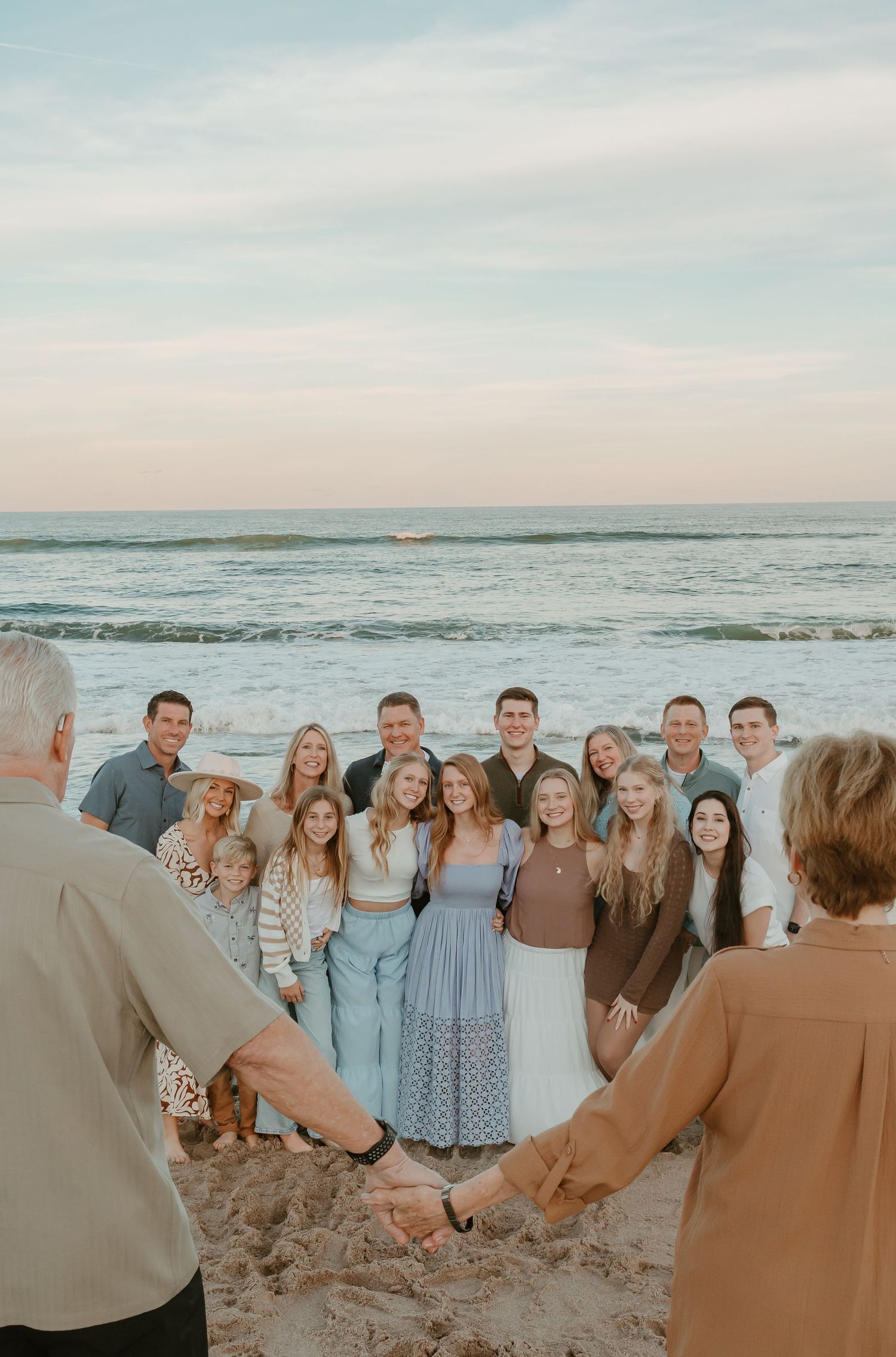 Multi-generational family gathering on beach wearing coordinated blue and brown tones.