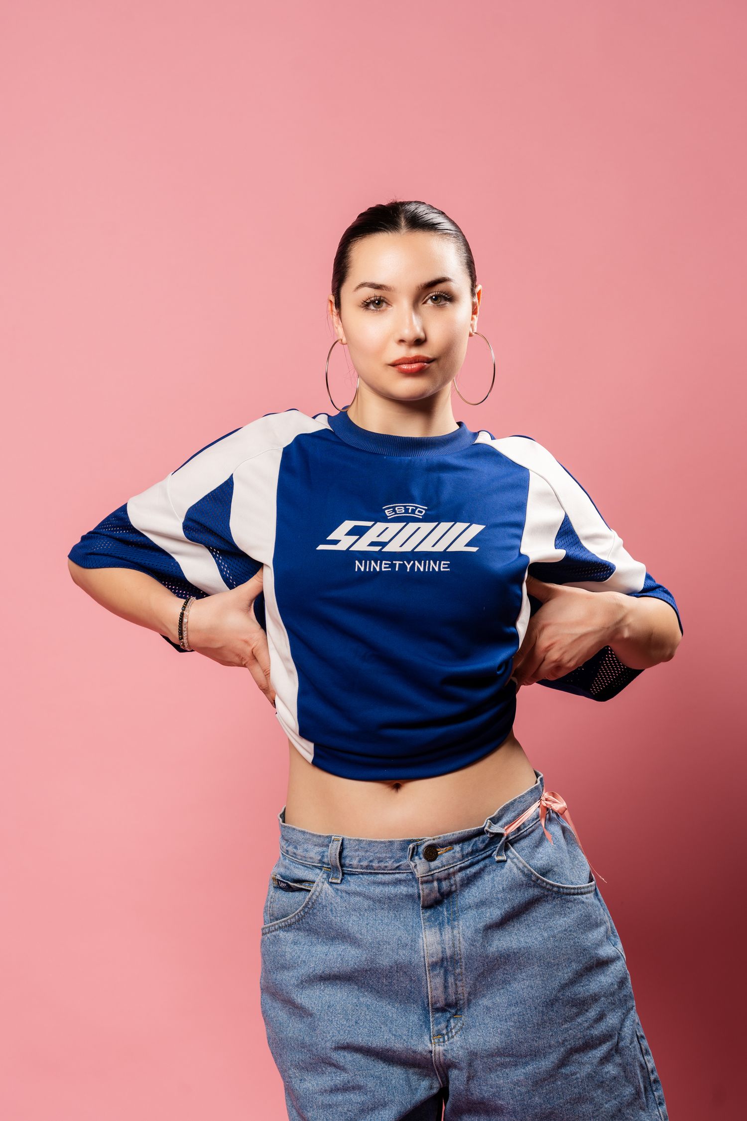 Model in blue crop top and jeans poses against pink background in dynamic fashion photo sequence.