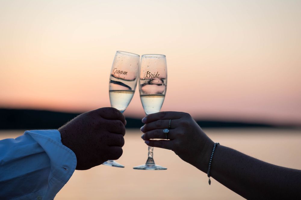 Two hands clink champagne glasses against a sunset sky.
