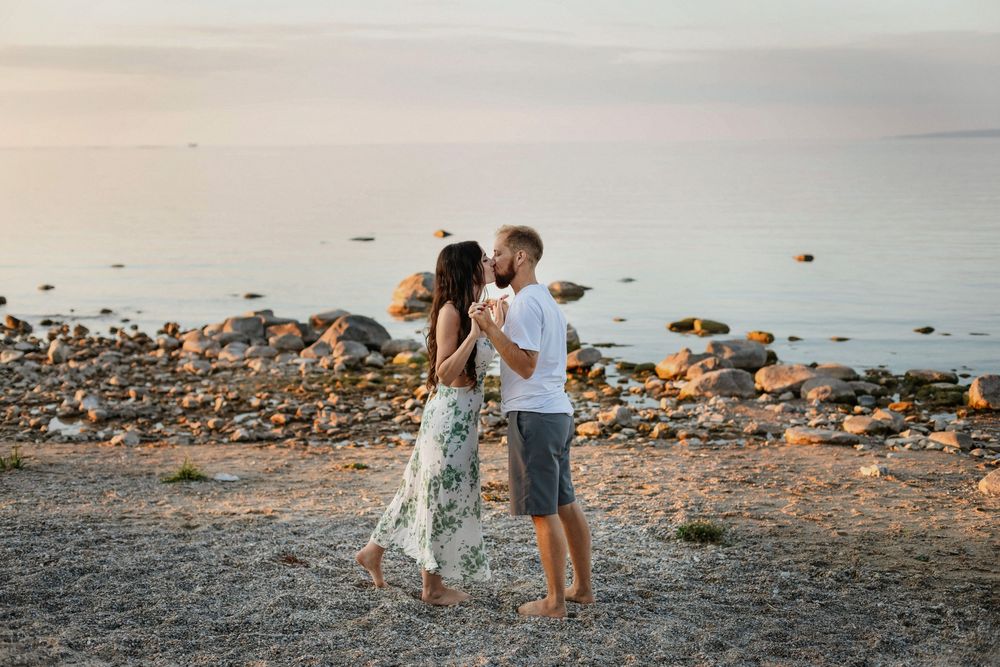 Romantic couple holding hands and kissing on a rocky beach at sunset with calm Lake Michigan waters in the background.