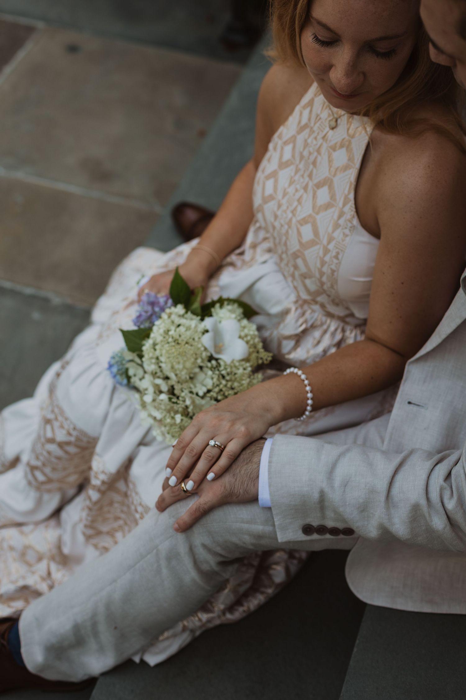 Close-up view of hands holding delicate white hydrangea flowers against a lace wedding dress.