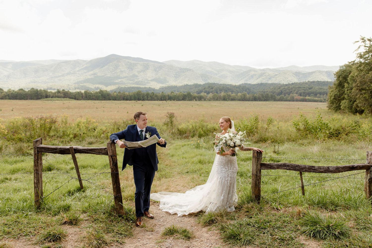 A couple poses by a rustic wooden fence with mountain views in the background.