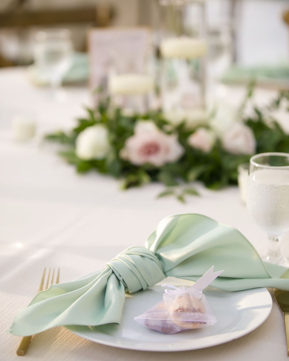 Elegant table setting with mint green napkin, gold flatware, and delicate pink rose on white china plate.