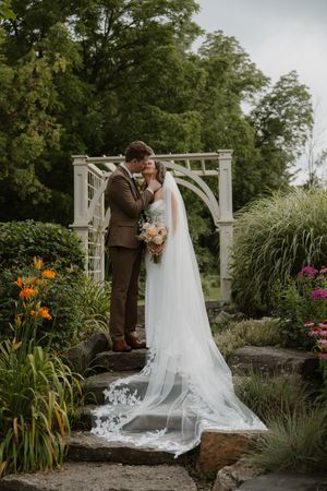 Newlyweds share an intimate moment in a lush garden setting with colorful flowers and a white arbor.