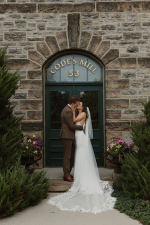 Romantic wedding couple poses in front of historic stone building with green doors and arched entrance.