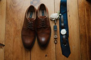 A collection of men's dress shoes and accessories arranged against a rustic wooden wall.