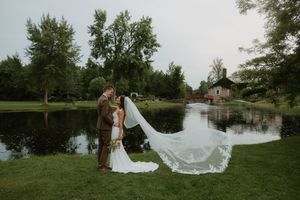 A couple shares a romantic moment by a serene pond as a long white veil flows dramatically in the breeze.