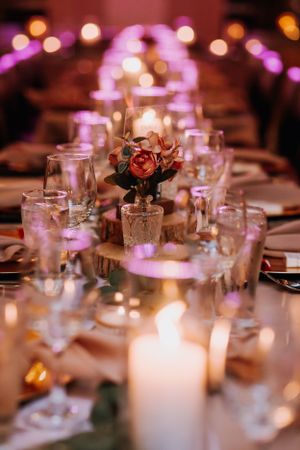 Romantic table setting with candles and rose centerpieces in purple ambient lighting.