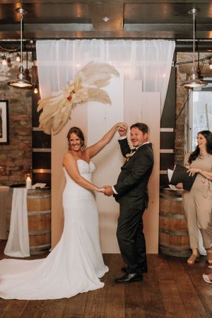 Wedding couple dancing in front of white backdrop with dried palm leaf decor.