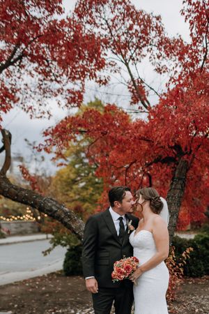 A couple shares a romantic moment under vibrant red autumn maple trees on their wedding day.