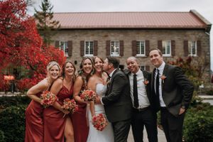Wedding party in burgundy dresses and black suits pose together in front of historic stone building.