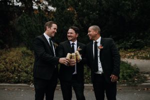Groomsmen laugh together while sharing drinks outdoors during wedding celebrations.