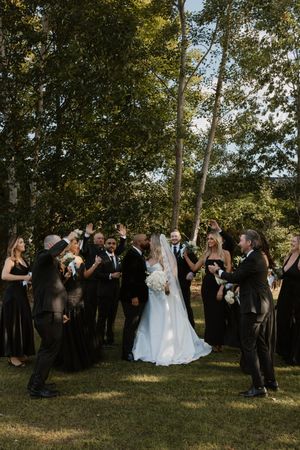 Wedding guests in formal attire gather outdoors under trees during a ceremony celebration.