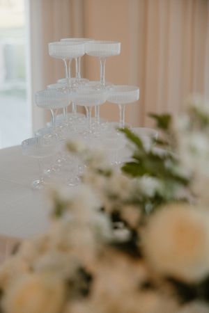 Elegant champagne glasses arranged in tiers on a white tablecloth with soft floral decorations in the foreground.