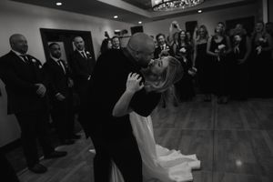 A couple shares a romantic dip during their first dance at a wedding reception while guests watch from the sidelines.