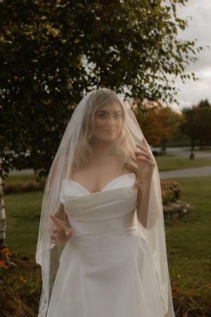 Close-up details of a bride's white wedding dress with delicate veil in an autumn outdoor setting.