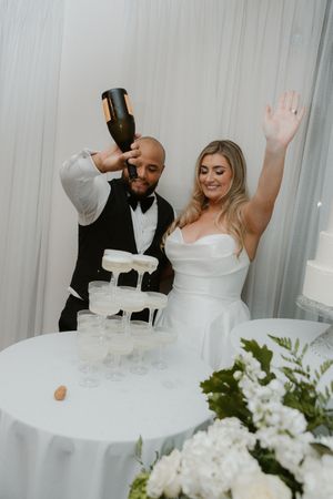Wedding reception table with white linens and floral centerpieces as guests celebrate with raised arms.