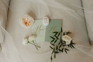 Elegant wedding details with white roses, greenery, and delicate fabric draped across a soft neutral background.