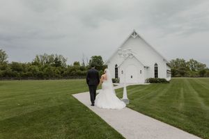 A modern white barn wedding venue sits on a lush green lawn under an overcast sky.