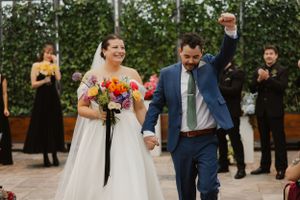 A joyful couple celebrates during their wedding ceremony while attendants in black look on from behind.