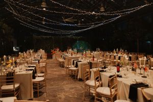 Elegant wedding reception venue with string lights overhead and rows of wooden chairs at white-clothed tables.