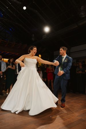 A couple dances energetically on a wooden dance floor at their wedding reception.