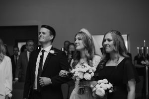Wedding guests dressed in formal attire smile and watch during a ceremony.