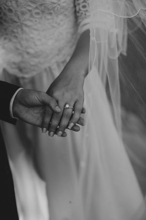 Black and white close-up of couple holding hands showing wedding ring.