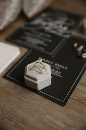 Wedding rings displayed in a white hexagonal ring box sitting on black stationery on a wooden surface.