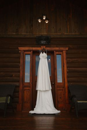 Elegant white wedding dress hanging on wooden cabin door.