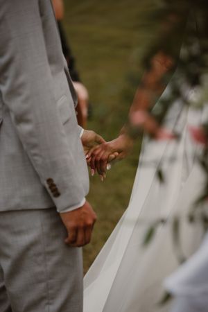 Close-up of couple holding hands during outdoor wedding ceremony.