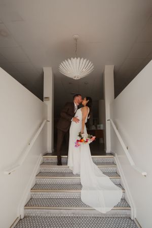 Wedding couple sharing romantic moment on staircase under elegant chandelier.