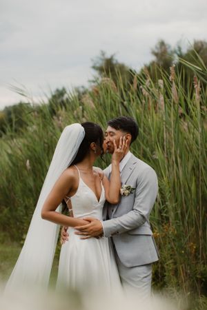 A romantic wedding portrait of a couple embracing in front of tall reeds.