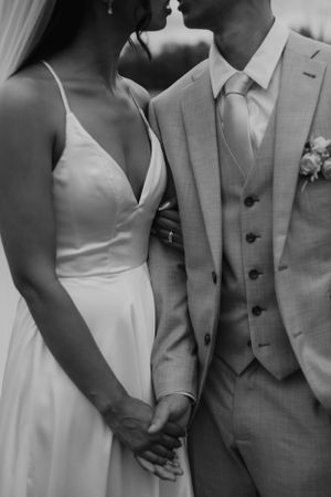 A black and white close-up of a bride and groom showing elegant wedding attire details.