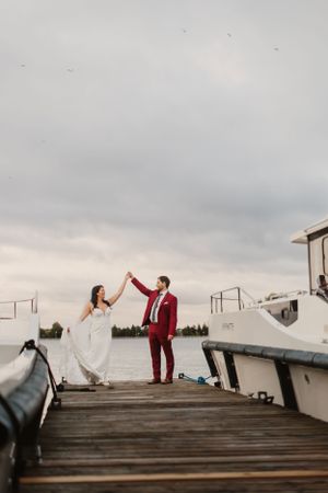 Newlyweds sharing joyful moment on wooden dock at sunset.
