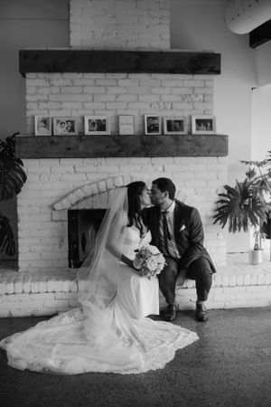Classic black and white wedding photo in front of white brick fireplace with vintage decor.