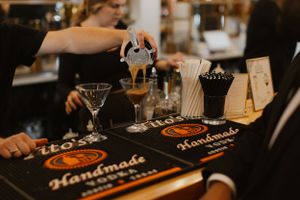 Bartender pouring cocktails at bar with handmade drink menu displayed.