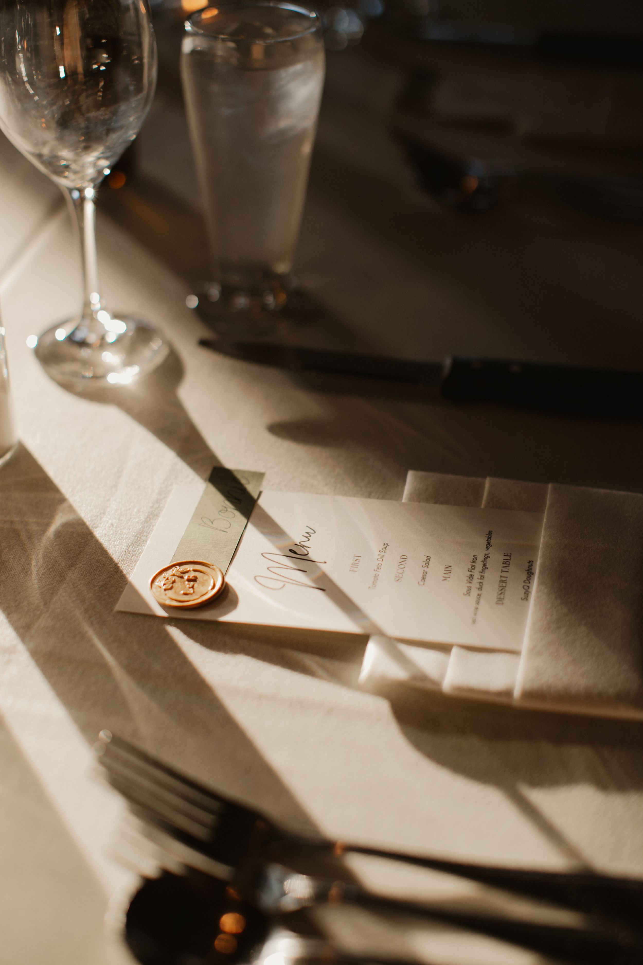 Close-up of wine glass and menu with wax seal on elegant place setting.