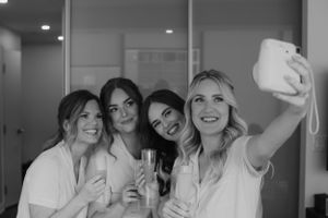 Group of friends in white robes taking a celebratory selfie with champagne glasses in hand.