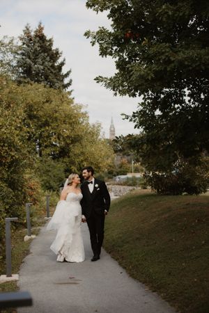Wedding couple walking hand in hand on path surrounded by autumn trees.
