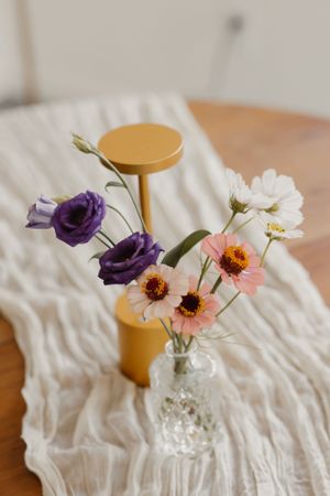 Delicate flower arrangement with purple and pink blooms in a clear vase on white fabric.