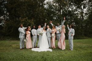 Wedding party celebrates on a lawn with bridesmaids in pink dresses and groomsmen in gray suits.