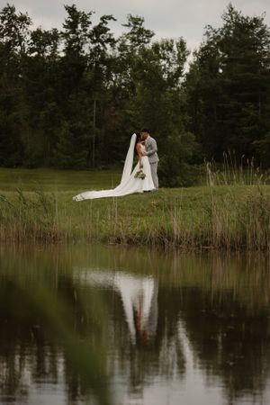A romantic wedding portrait of a couple by a lake with their reflection in the water.