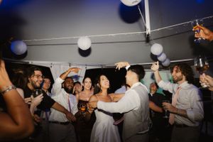 Wedding reception dance party with celebratory crowd under decorative lights on dance floor.