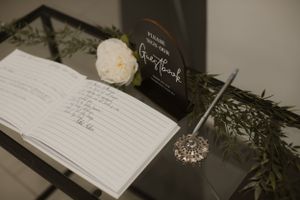 Wedding guest book with a white rose and calligraphy sign displayed on a dark surface.
