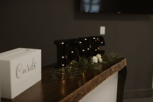 Wedding decor featuring illuminated marquee letters and greenery on a rustic wooden shelf.