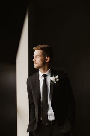 A formal portrait of the groom in a dark suit with boutonniere against a dramatic light and shadow background.