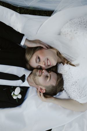 Wedding couple lying together on ground in formal attire.