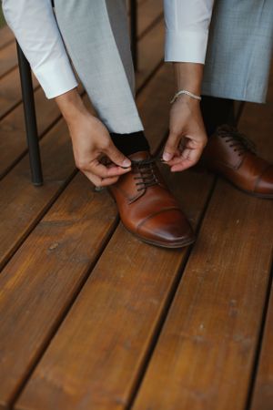 Hands tying brown leather dress shoes on wooden deck.